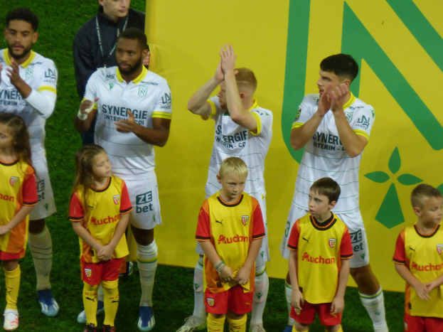 Eine Gruppe von Fußballspielern in Uniformen klatscht feierlich auf einem Ligue-1-Feld mit einem "Ligue-1"-Schild im Hintergrund.