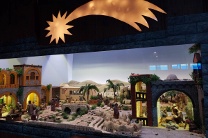 Eine Krippe-Ausstellung im Museum mit Menschen, Tieren, Häusern, Bäumen und anderen Gegenständen und einer Lampe, die die Szene von oben beleuchtet.