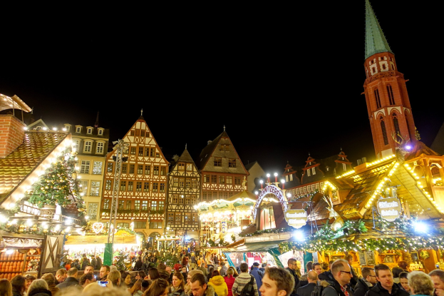 Ein geschäftiger Weihnachtsmarkt in Nürnberg, Deutschland mit Menschen um geschmückte Stände, Gebäuden mit Fenstern, einem Uhrenturm und einem dunklen Himmel.