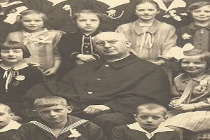 Ein Schwarz-Wei├č-Foto eines strengen Mannes, der in der Mitte sitzt und von einer Gruppe bewundernder Kinder umgeben ist.