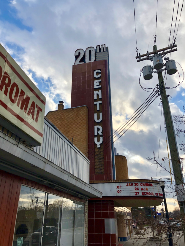 Au├čenansicht des 20th Century Theatre in Detroit, Michigan, mit Glasw├Ąnden, Namensschildern, umgeben von B├Ąumen und Strommasten mit Dr├Ąhten unter einem bew├Âlktem Himmel.