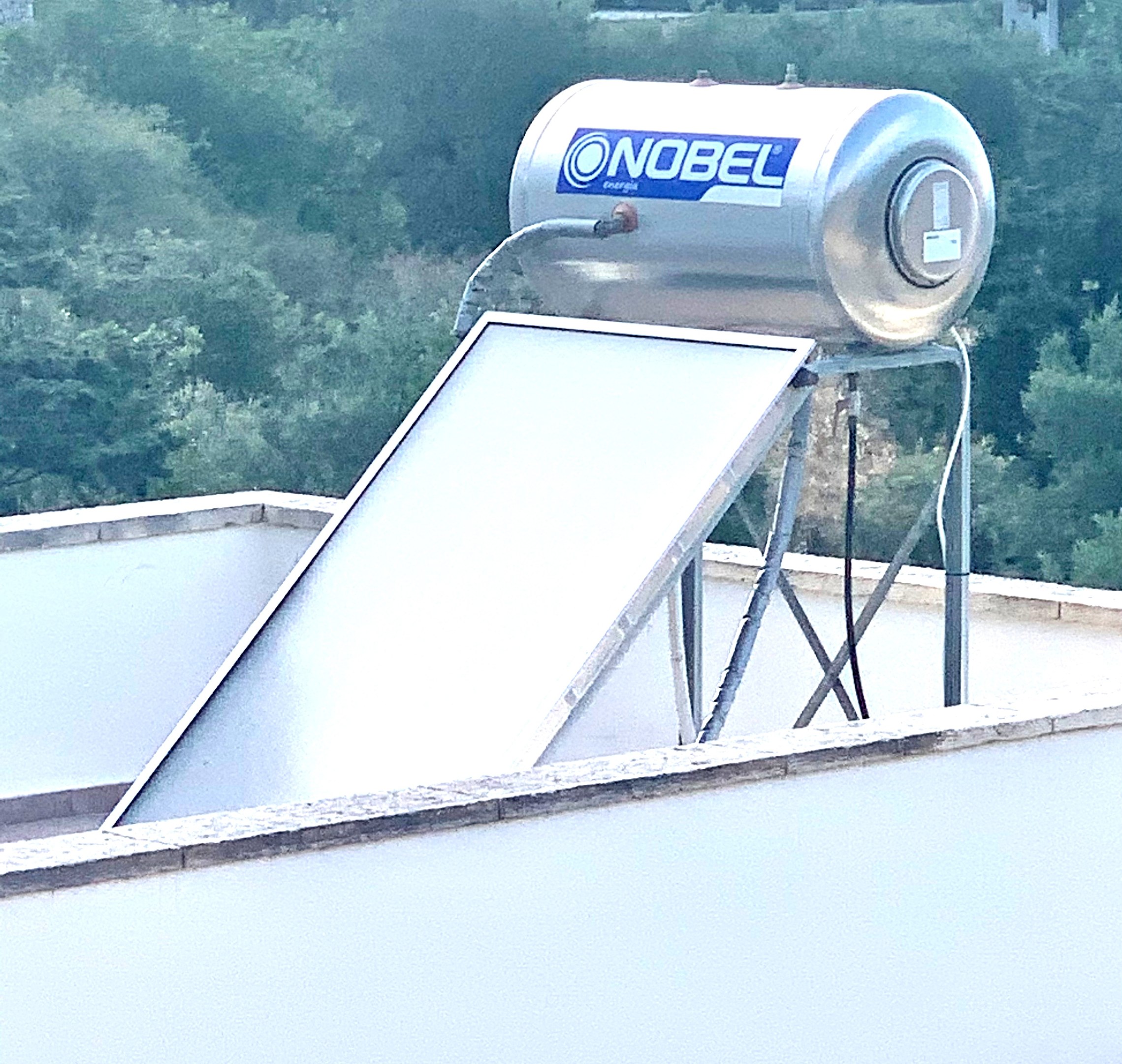 Solarwassererhitzer mit Speicherbehälter auf dem Dach eines Gebäudes montiert, Bäume im Hintergrund sichtbar.