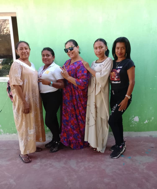 Eine Gruppe von Frauen steht gemeinsam vor einer grünen Wand mit einem Fenster auf der linken Seite und nimmt an einem Internationalen Frauentag-Event teil.