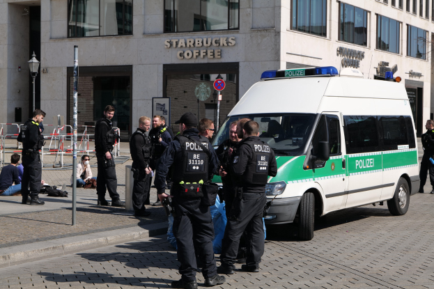Polizeibeamte vor einem Starbucks-Café mit einem Van auf der rechten Seite und Menschen auf der linken Seite vor einem Hintergrund aus Gebäude, Schilder, Laterne und Zaun.
