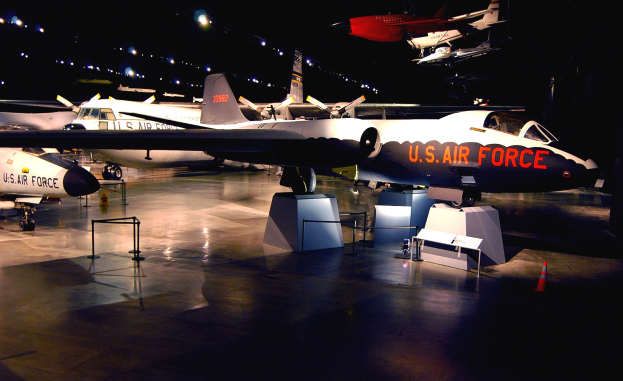 Eine Gruppe von Kampfflugzeugen in einem schwach beleuchteten Museum mit St├Ąnden, Verkehrskegeln und anderen Bodenobjekten, die von fokussiertem Licht beleuchtet werden.
