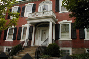 Ein Gebäude mit Glasfenstern und weißen Rändern, das eine Treppe mit schwarzen Zäunen auf beiden Seiten hat, flankiert von Bäumen.