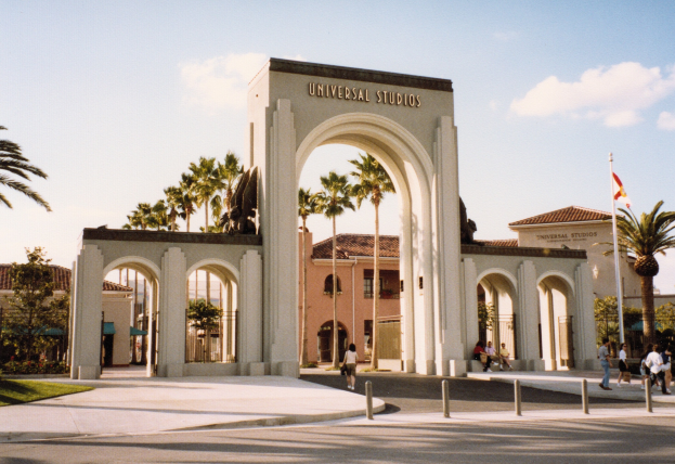 Eingang von Universal Studios Hollywood mit einem Bogen, einer Statue, Menschen, Bäumen, Gebäuden und einem Fahnenmast.