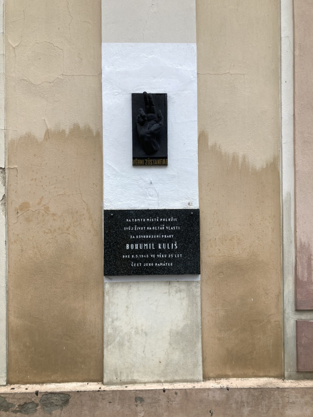 Schwarze Tafel an einem Gebäude mit einer Hand darauf, beschriftet mit Text, wahrscheinlich ein Holocaust-Mahnmal.