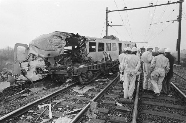 Ein Schwarz-Weiß-Bild von einer Zugkollision auf den Gleisen mit Einsatzkräften in Helmen und einem Hintergrund von Strommasten, Bäumen, Gebäuden und einem klaren Himmel.