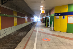 Ein Bahnhof in Berlin, Deutschland, mit einem Zug auf den Gleisen, beleuchtet von Deckenlampen, Graffiti an der linken Wand und ein paar Gegenständen auf der rechten Seite.